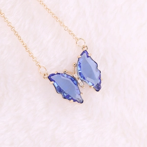 Detailed macro shot of a blue crystal butterfly pendant on a gold chain over white faux fur