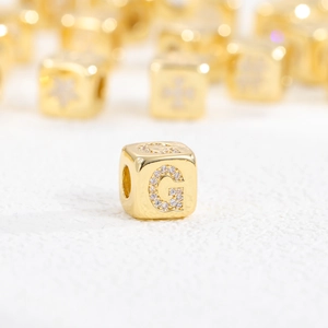 Macro shot of 18k gold plated cube bead with zircon letter G for jewelry making