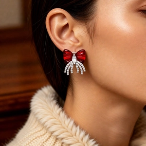 Detail of red bow earring with zircon tassels worn by model in a warm indoor setting