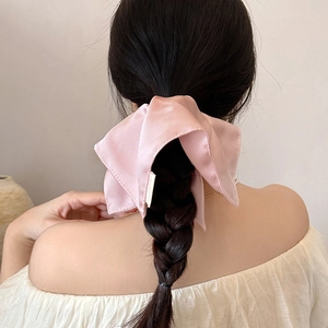 Pink satin bow scrunchie accessory worn on a low ponytail for an elegant hair styling look