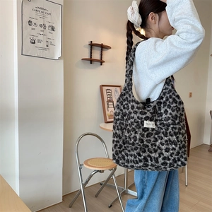 Black and grey leopard print plush tote bag shown in a cozy lifestyle cafe setting