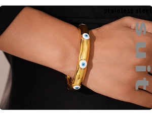 Close-up of golden stainless steel open bracelet with blue evil eye charms on a model