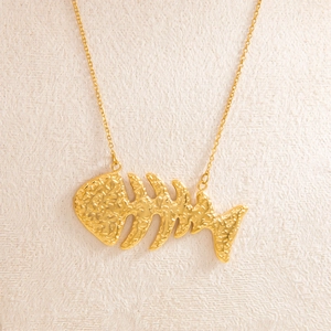 Close-up of 18k gold fishbone pendant showing detailed hammered texture on a fine chain