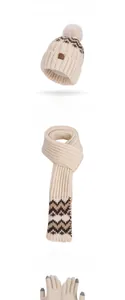 Detailed close-up of cream knit winter set including beanie with pompom, scarf and gloves
