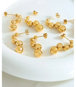 Minimalist gold gradient steel ball stud earrings displayed on a white ceramic plate