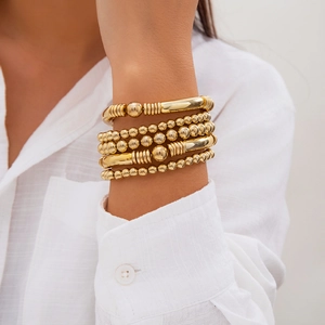 Close-up of stacked gold beaded bracelets with heart charms on model's wrist