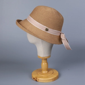 Khaki breathable knit bucket hat with pink ribbon and metal rose detail on wooden stand