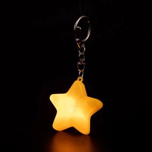 Luminous yellow star keychain glowing against a black background with a metal ring