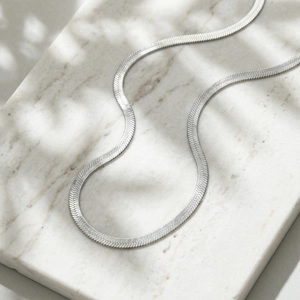 Detailed view of silver flat snake bone chain necklace on white marble surface