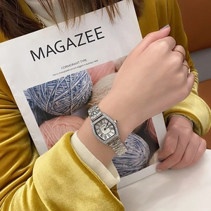 Detail of silver tonneau watch with crystal bezel worn by a model holding a magazine