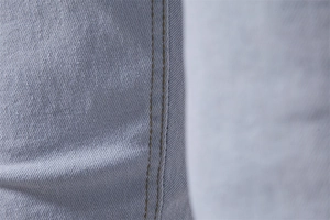 Detailed close-up of light blue denim fabric with reinforced yellow double-stitch seams