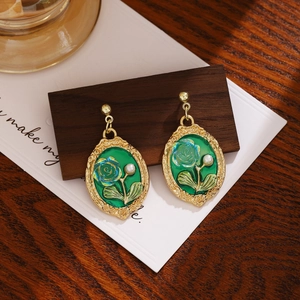 Detail of vintage emerald earrings with blue roses and white pearls on wooden base