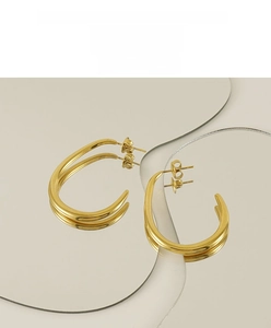 Close-up of polished 18K gold-plated U-shaped earrings on a reflective geometric mirror