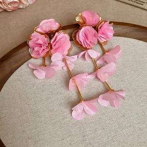 Close-up of pink chiffon flower tassel earrings on a wooden tray with dry flowers