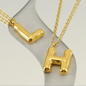 Macro view of golden bubble balloon L and H letter pendants on minimalist chains