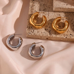 Detail of chunky gold and silver square-cut hoop earrings on neutral stone backdrop