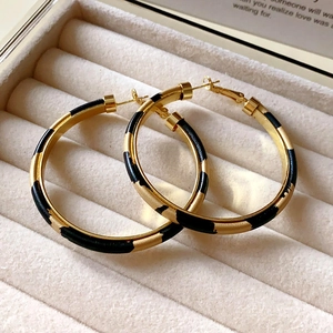 Close-up of C-shaped acrylic earrings with gold finish and black striped patterns in a box