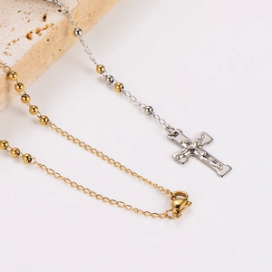 Detail showing two-tone gold and silver cross rosary necklace with metal beads on stone