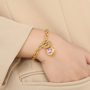 Detail of gold OT buckle bracelet featuring a purple satellite stone on a model's wrist