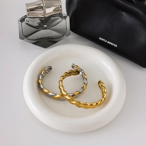 Close-up of twisted 18K gold and silver stainless steel bangles on a luxury tray