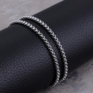 Close-up of a silver stainless steel box chain necklace on a black leather display stand