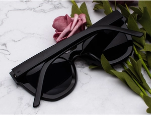 Detail of oversized black cat-eye sunglasses on white marble background with rose