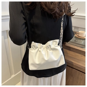Lifestyle shot of white pleated cloud bag with chain strap on a woman in elegant setting