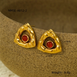 Macro view of triangle crinkled gold earrings with red natural stone on ceramic pot