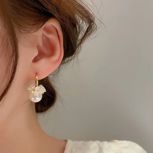 Detail shot of elegant white pearl flower earrings with gold accents worn by a model