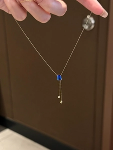 Détail d'un collier avec pendentif saphir bleu rectangulaire et fines chaînes dorées