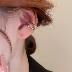 Close-up of gold bow ear cuff with zircon and pearl details worn on a model ear