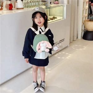 Cute green toddler canvas backpack with plush bunny doll on young girl in a shop