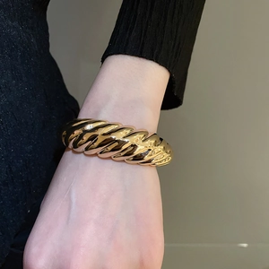 Close-up of a chunky twisted gold bangle with mirror polish finish on a model wrist