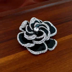 Macro shot of black enamel camellia brooch with sparkling rhinestones on wood