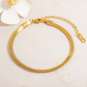 Close-up of golden flat snake chain bracelet on marble surface with flower petals