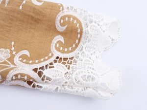 Detail of camel fabric with white floral embroidery and delicate lace trim on the garment