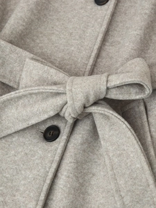 Detail of wool coat featuring a waist belt tied in a bow and dark button accents
