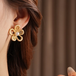 Gros plan d'une mannequin portant des boucles d'oreilles fleur évidée dorée et perle