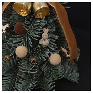 Close-up of miniature Christmas tree with golden bells, plush rabbit, and velvet ribbons