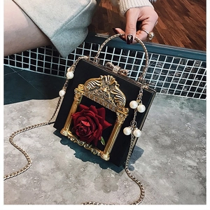 Detail of black box bag with red rose, gold frame, and luxury pearl chain handle