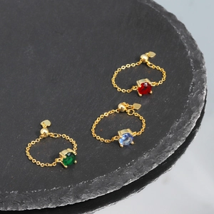 Adjustable gold chain rings with red blue and green gems on a stone platter