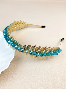 Close-up of golden leaf headband with blue crystal beads on a beige texture background