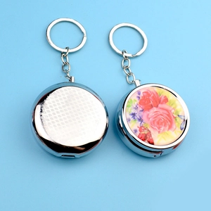 Macro detail of round metal pill box keychain featuring a colorful peony floral pattern