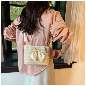 Close-up of woven straw bucket bag featuring a large white mesh bow and leather strap