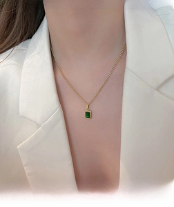 Close-up of emerald green rectangle pendant on gold chain necklace worn by model