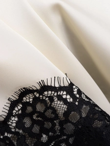 Detailed close-up of cream satin fabric with black eyelash lace trim stitching