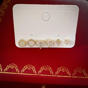Détail de trois paires de boucles d'oreilles cœur dorées avec zircon blanc et émail sur carte