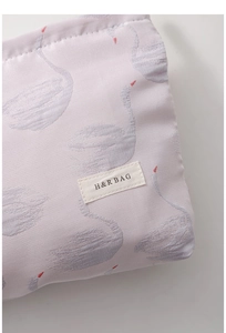 Detailed view of jacquard swan pattern and fabric label on a purple cosmetic bag