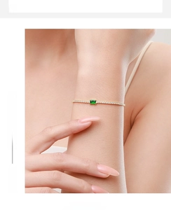Detail of gold bracelet with rectangle green zircon and clear stones on woman wrist