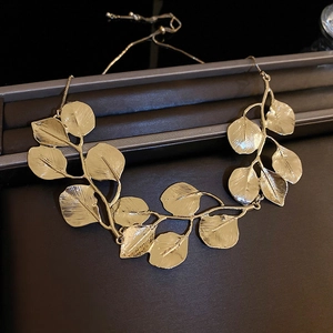 Detailed close-up of a gold metal leaf necklace set on a premium dark presentation box